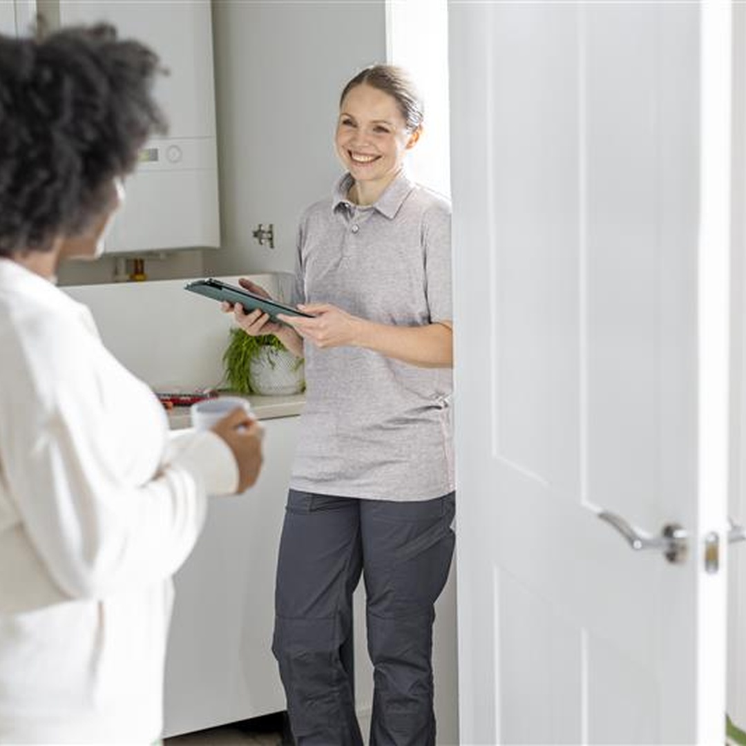 Home energy engineer visiting a customer at home and using a tablet while discussing the household’s energy services.