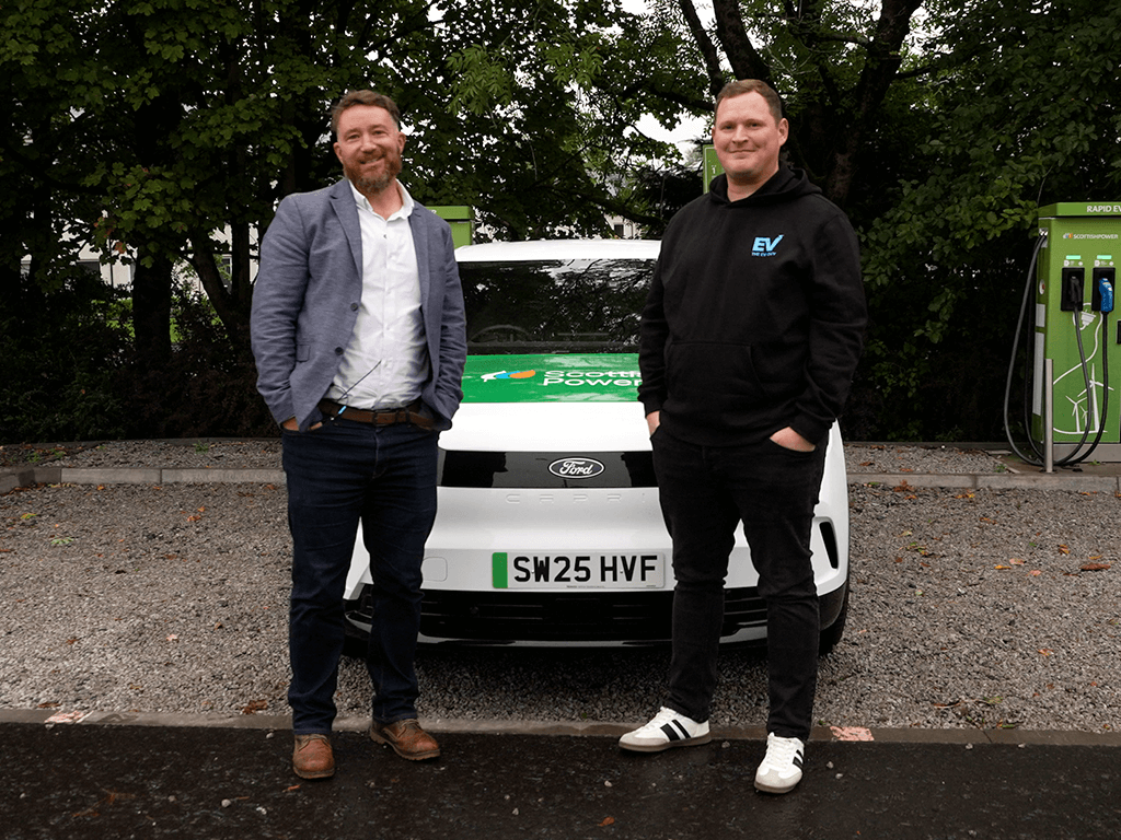 Two people stand in front of a white Ford electric vehicle branded with the ScottishPower logo, promoting electric vehicle expertise and sustainable energy solutions.