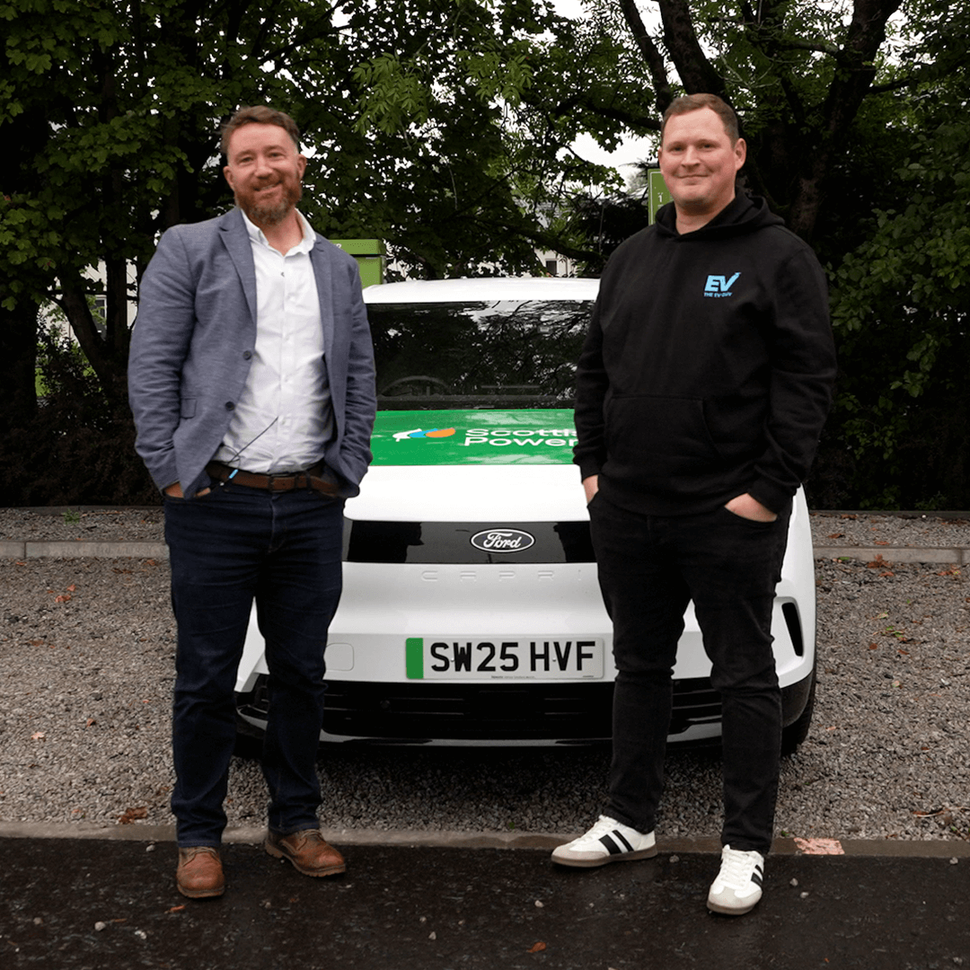 Two people stand in front of a white Ford electric vehicle branded with the ScottishPower logo, promoting electric vehicle expertise and sustainable energy solutions.