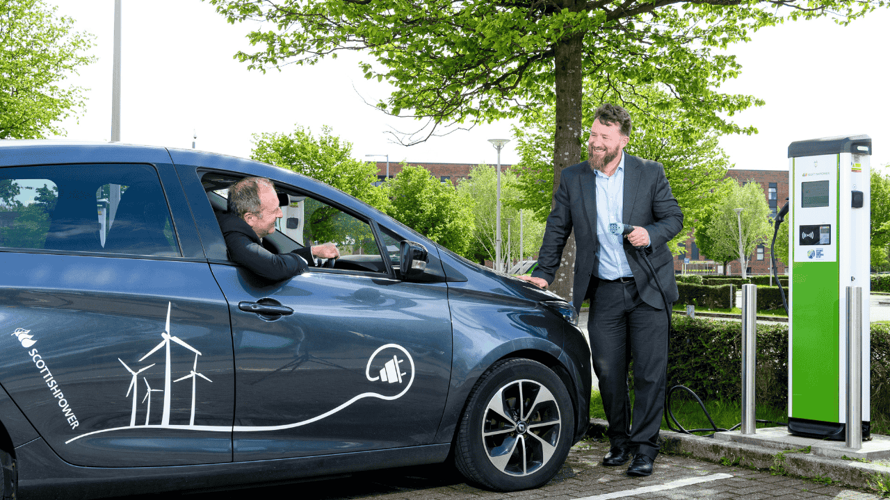 Electric vehicle driver speaking with a representative beside a public EV charging station, highlighting electric vehicle charging infrastructure and support for EV drivers.