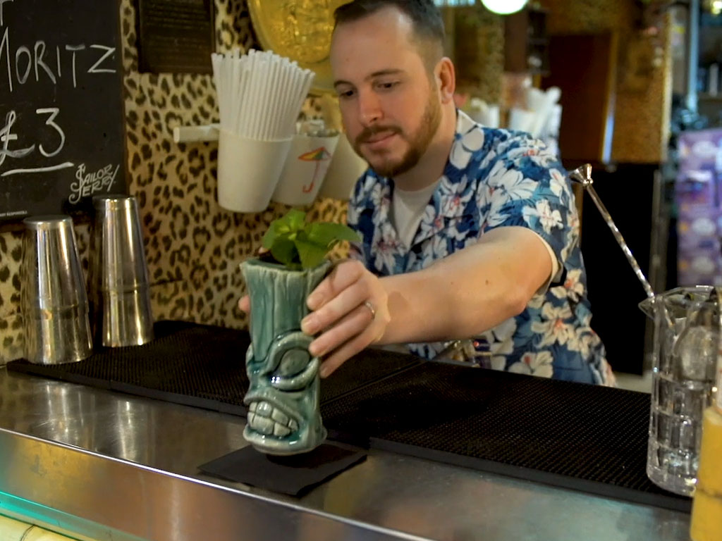 Person preparing a drink behind a bar, highlighting hospitality services, customer experience and support for local businesses in the food and drink sector.