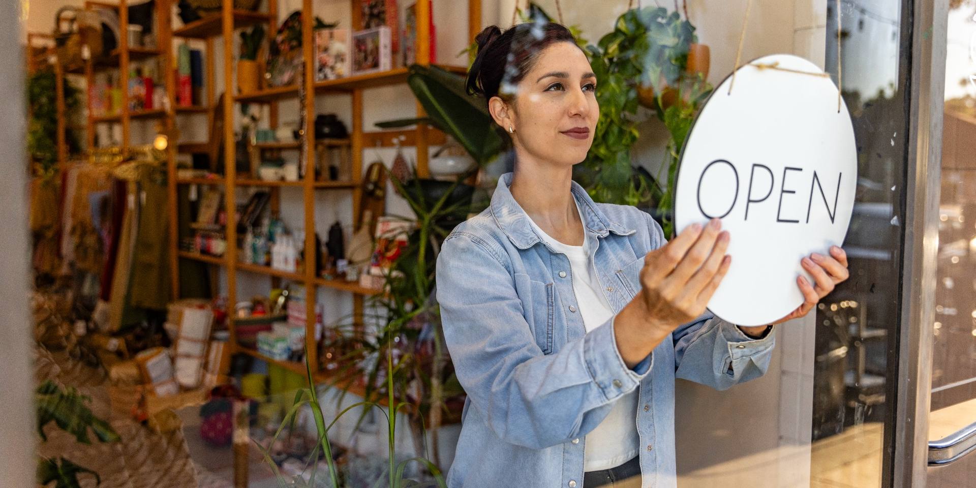 Small business owner placing an open sign in a shop window, preparing the retail business to welcome customers and begin trading.