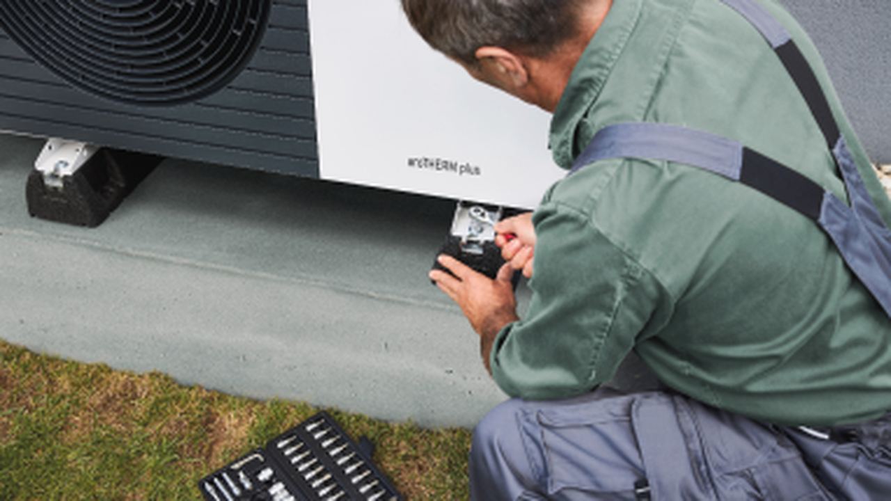 Worker installing air source heat pumps outside a house