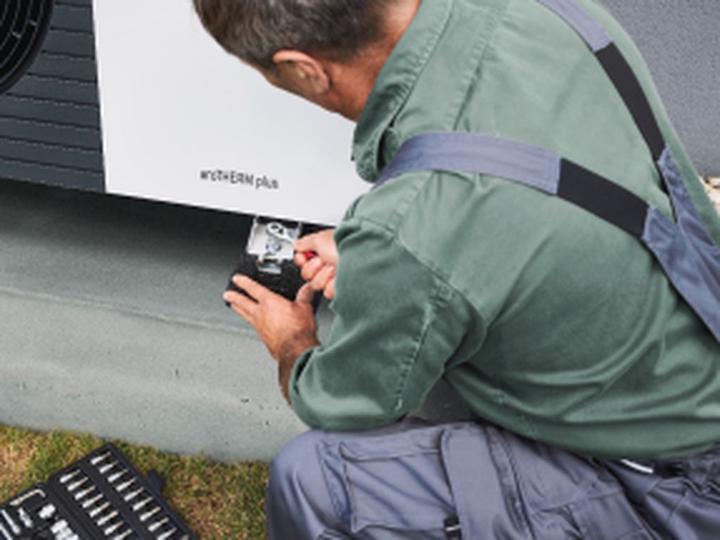 Worker installing air source heat pumps outside a house