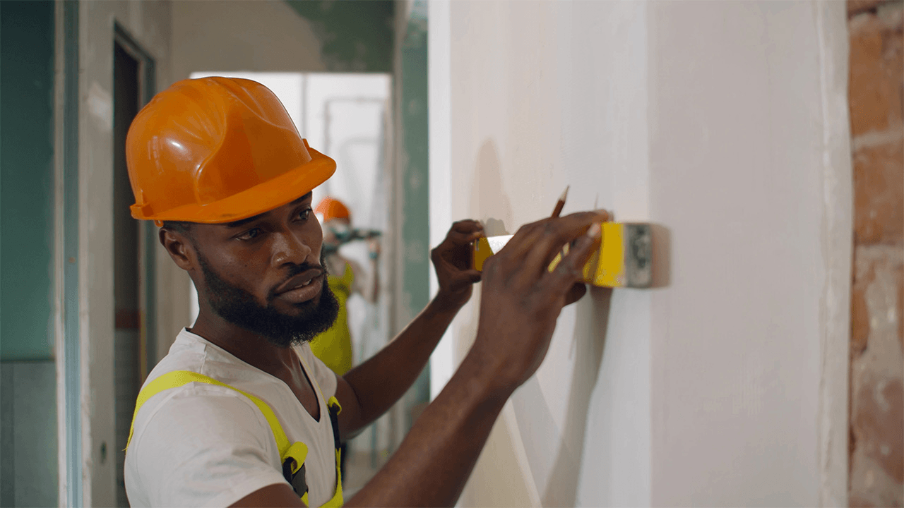 Construction worker measuring and marking an interior wall during a building renovation project.