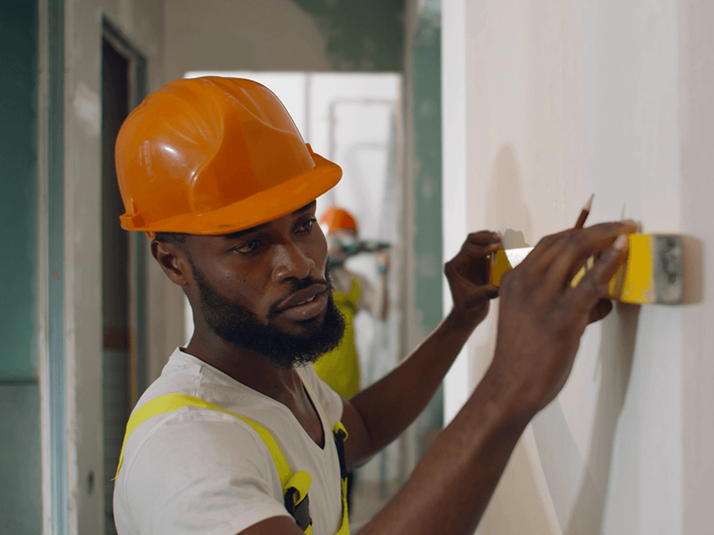 Construction worker measuring and marking an interior wall during a building renovation project.