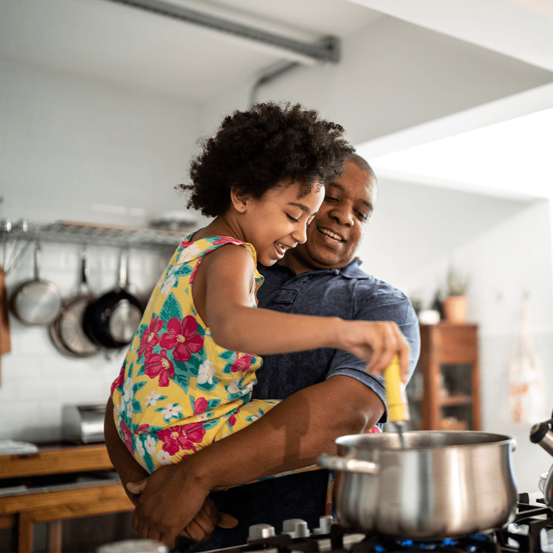Child stirring a pot while cooking with an adult in a kitchen.