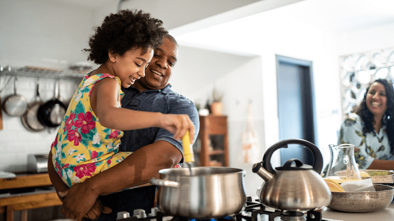 Child stirring a pot while cooking with an adult in a kitchen.