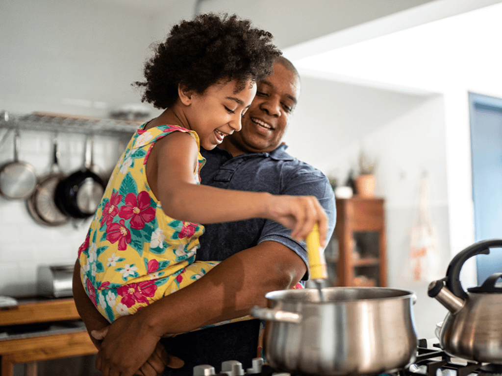 Child stirring a pot while cooking with an adult in a kitchen.