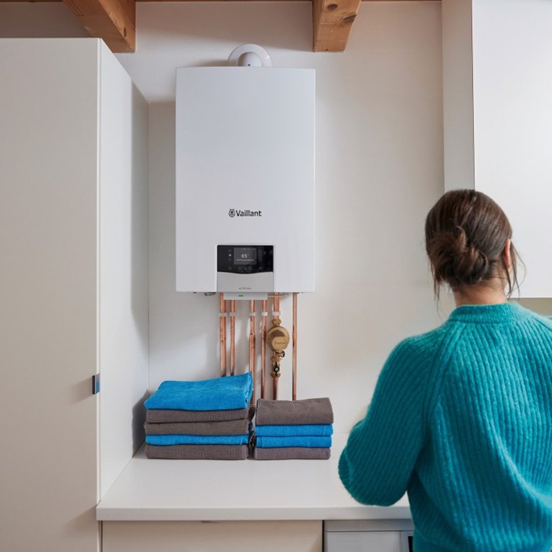 Wall‑mounted boiler installed above a counter in a utility room, with a person standing beside it.