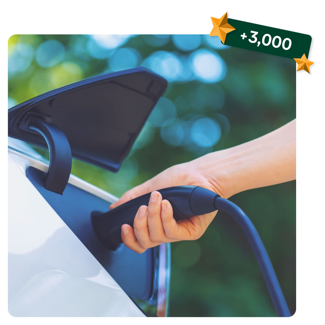 Hand plugging an electric vehicle charging cable into a white car, with a green badge with ‘+3,000’ in the top corner.