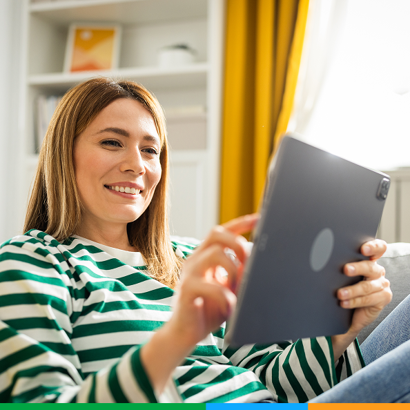A smiling woman in a striped top sitting on a sofa with a tablet