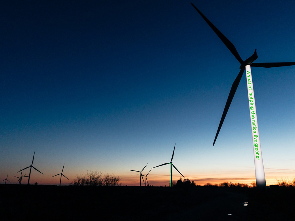 The Whitelee windfarm at sunset, with 'A year of helping the nation live greener' projected on a wind turbine