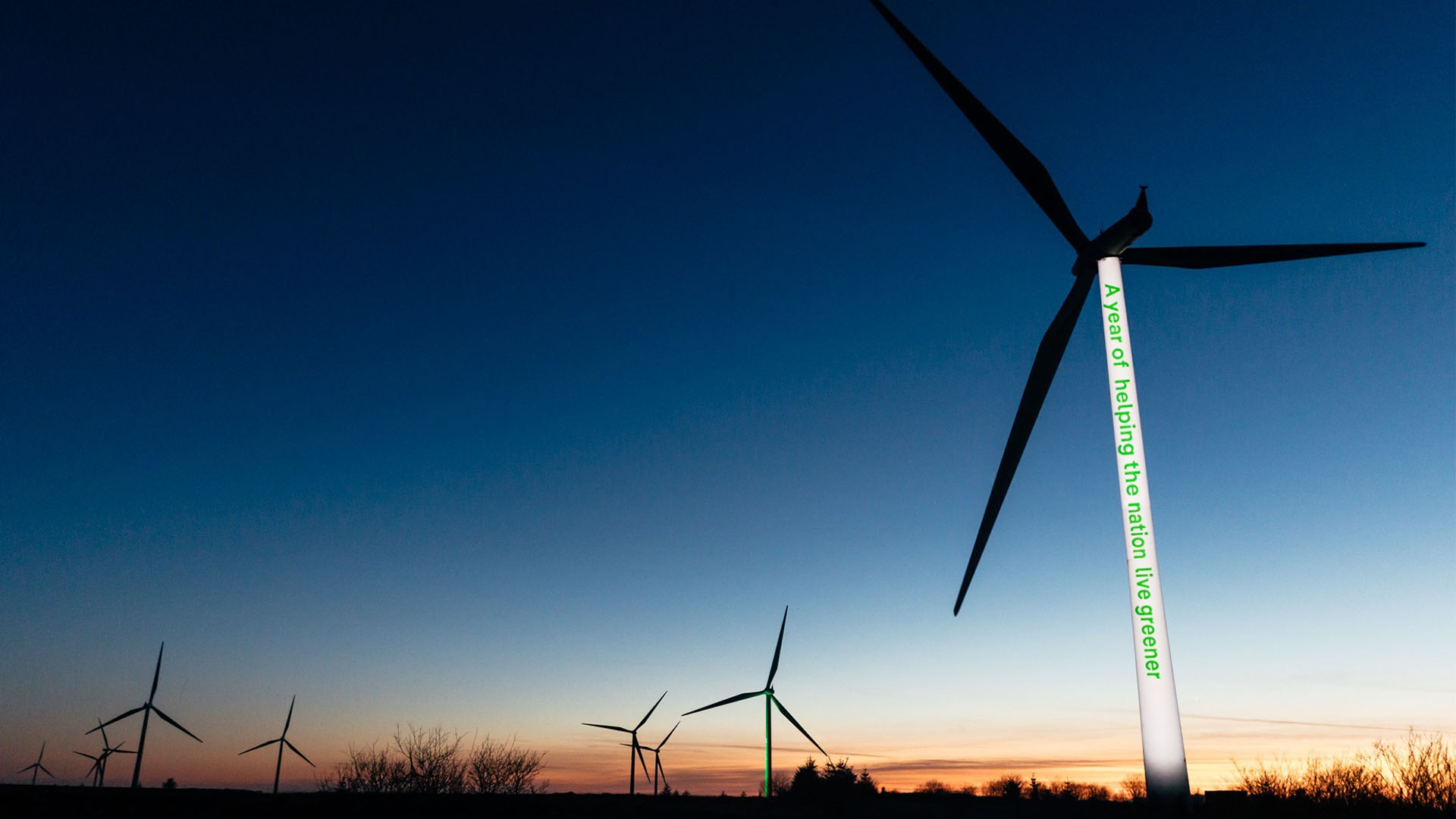 The Whitelee windfarm at sunset, with 'A year of helping the nation live greener' projected on a wind turbine