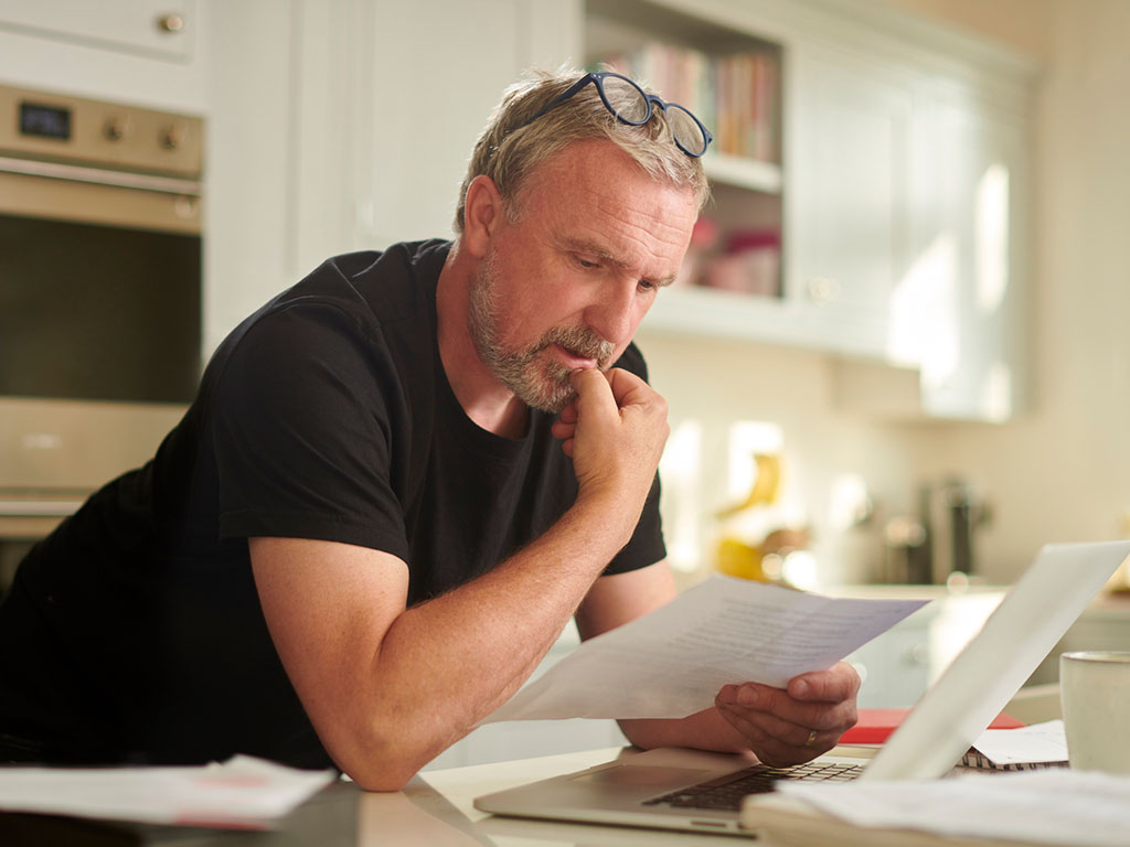 A ScottishPower customer sitting at their kitchen table reviewing a printed energy bill with their laptop nearby.