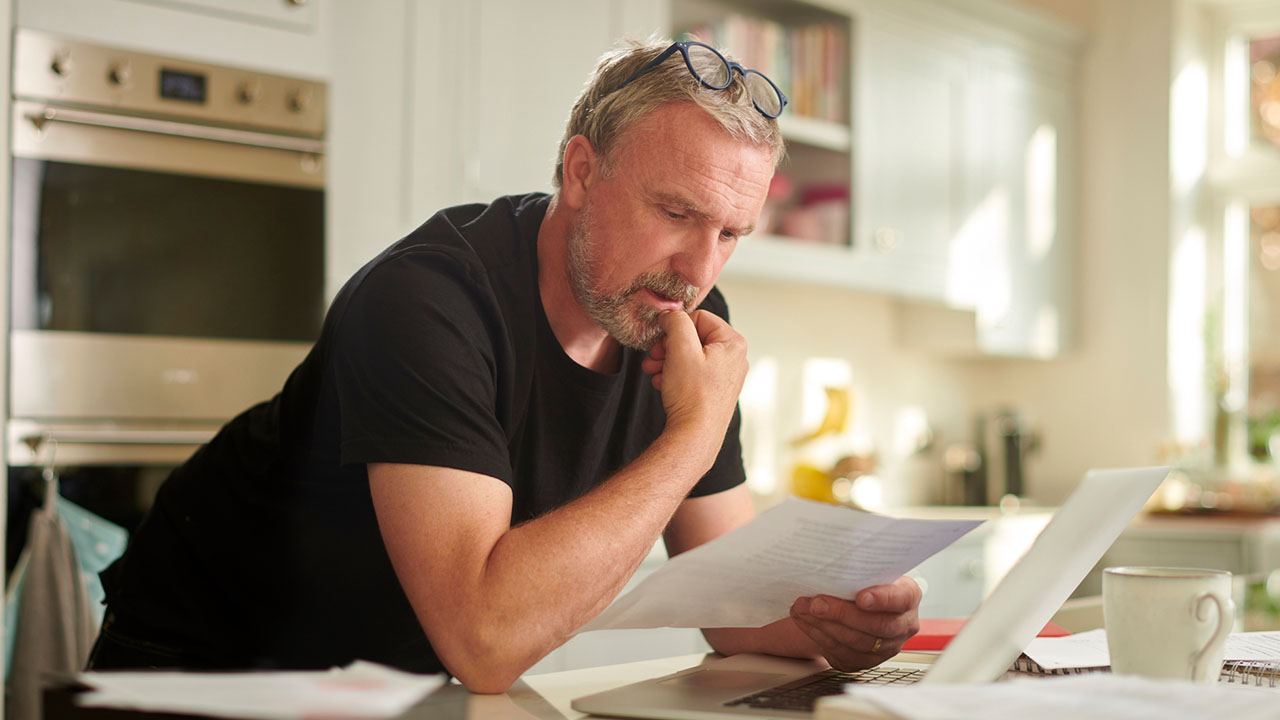 A ScottishPower customer sitting at their kitchen table reviewing a printed energy bill with their laptop nearby.