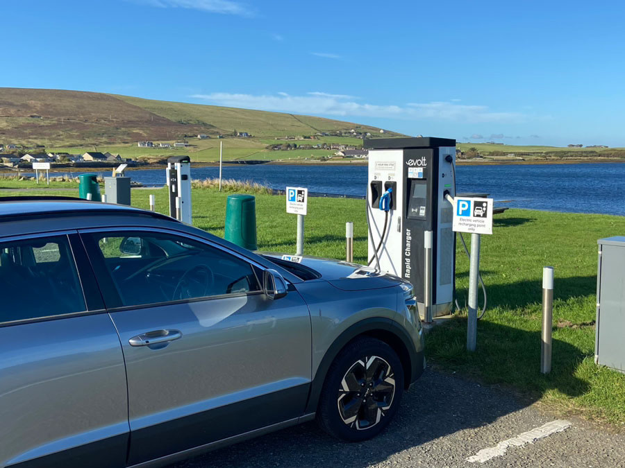 Electric car charging at an outdoor EV charging station beside a lake in a rural area.