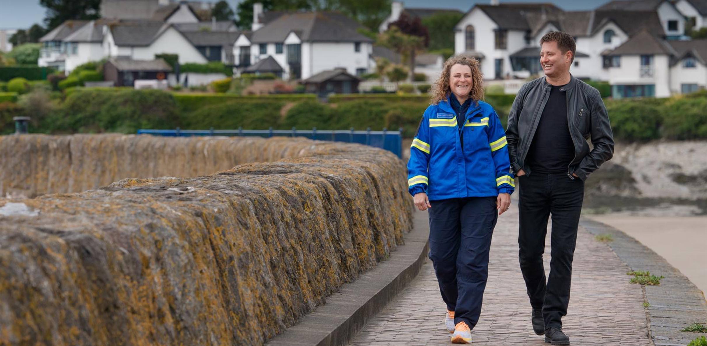 George Clarke walking beside ScottishPower customer Rebecca on a path along the beach