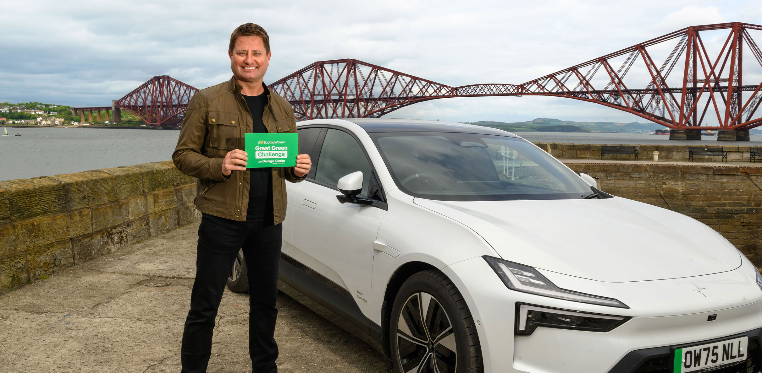 George Clarke in a white electric car sitting in front of the Fourth Road Bridge