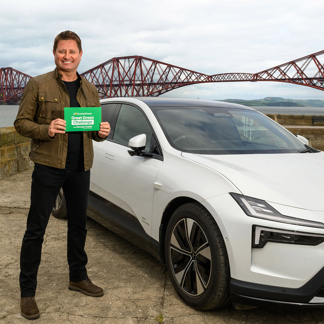 George Clarke in a white electric car sitting in front of the Fourth Road Bridge