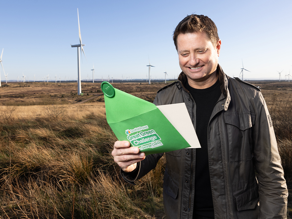 George Clarke opening green envelope announcing the Great Green Challenge with ScottishPower, in front of a wind farm