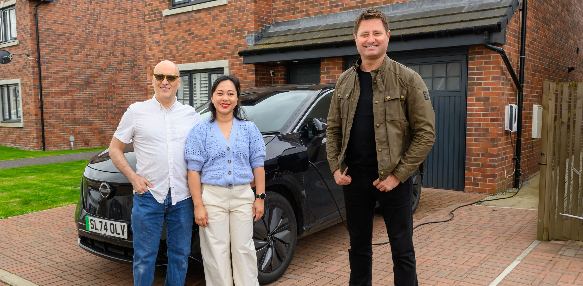 George standing outside on a driveway with a couple who are ScottishPower customers. They are standing next to their electric car.