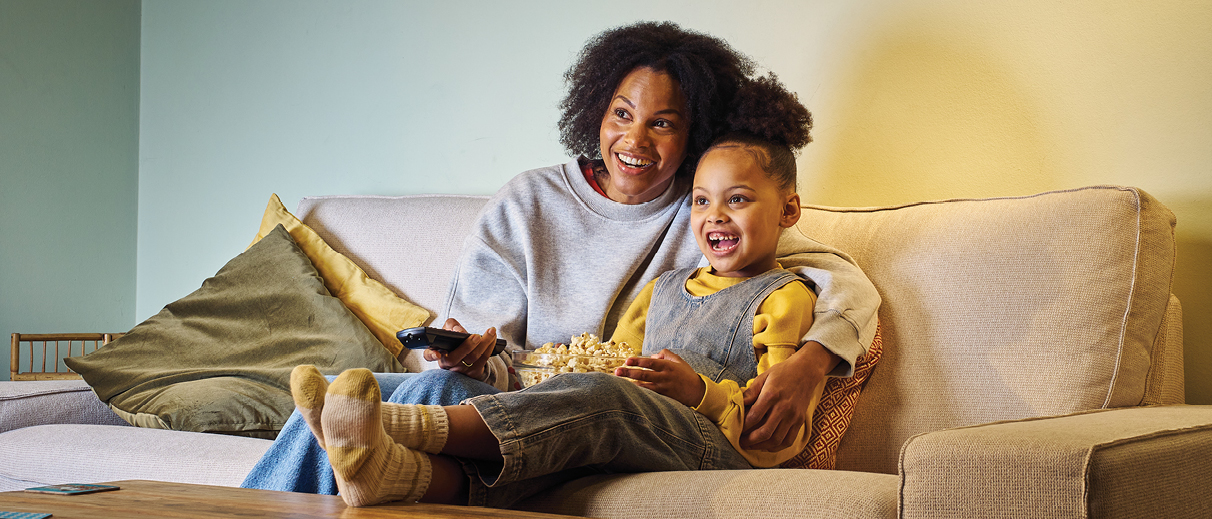 Woman with her daughter on the sofa smiling and watching the TV