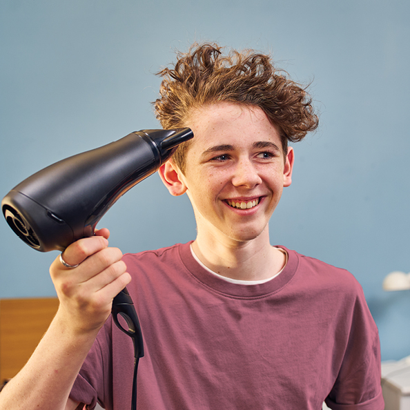 Boy smiling while blowdrying his hair with a hairdryer