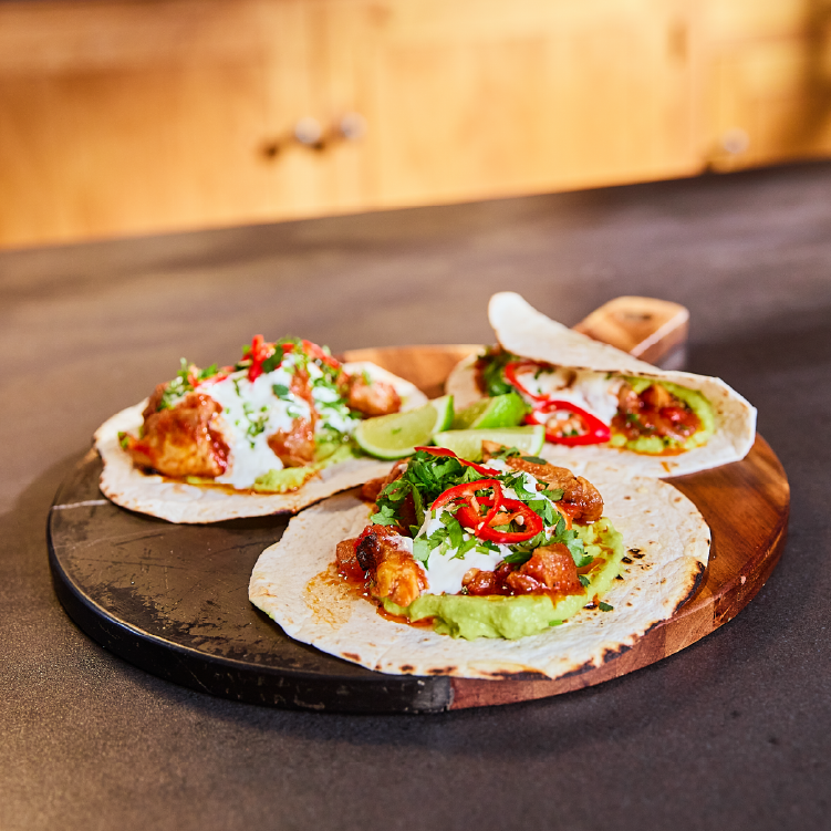 Three spicy chipotle chicken tacos placed on a circular wooden board.