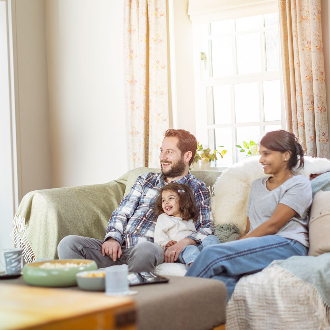 Man and woman sitting on a sofa with their daughter smiling