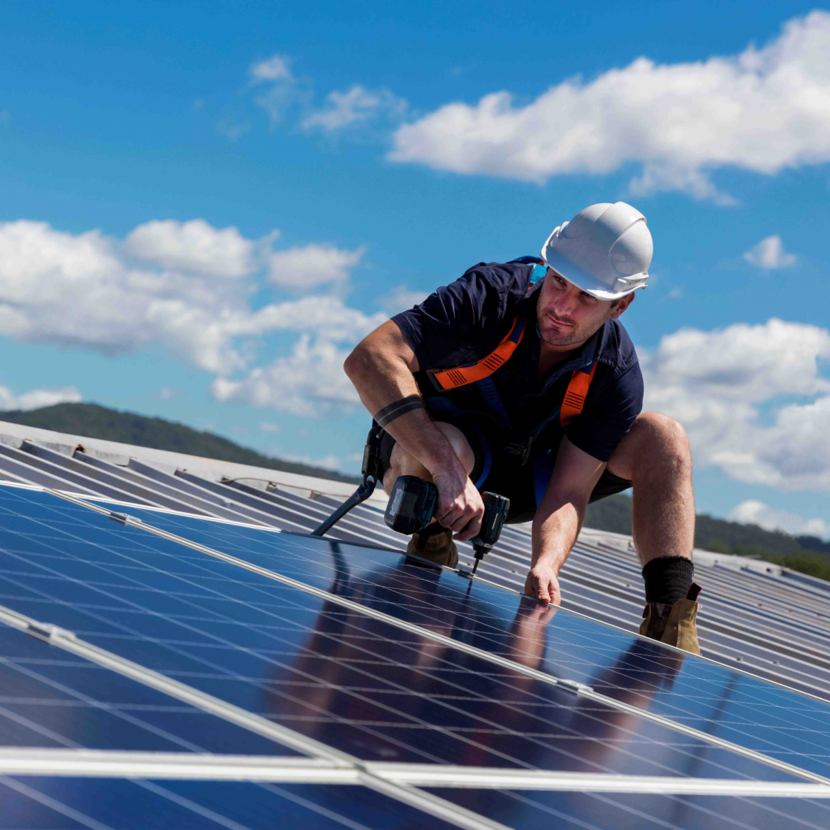 Man wearing a hard hat installing solar panels on a roof