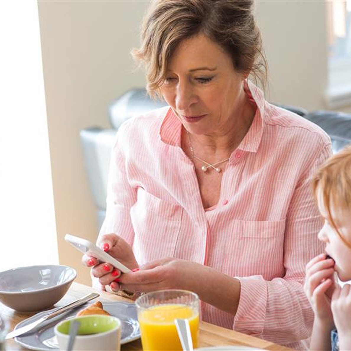 women sitting at her dining table eating breakfast and looking at her phone